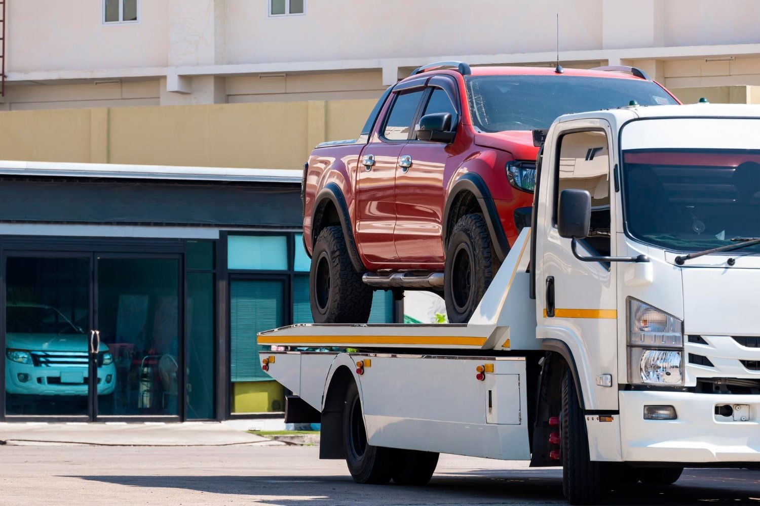 Tow truck carrying a red ute on its tray